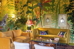 A room with a sofa, armchairs, a glass coffee table, and a wall with a nature-themed mural. - Finca Aal Cachucho Hotel Rural (San Agustin del Guadalix)