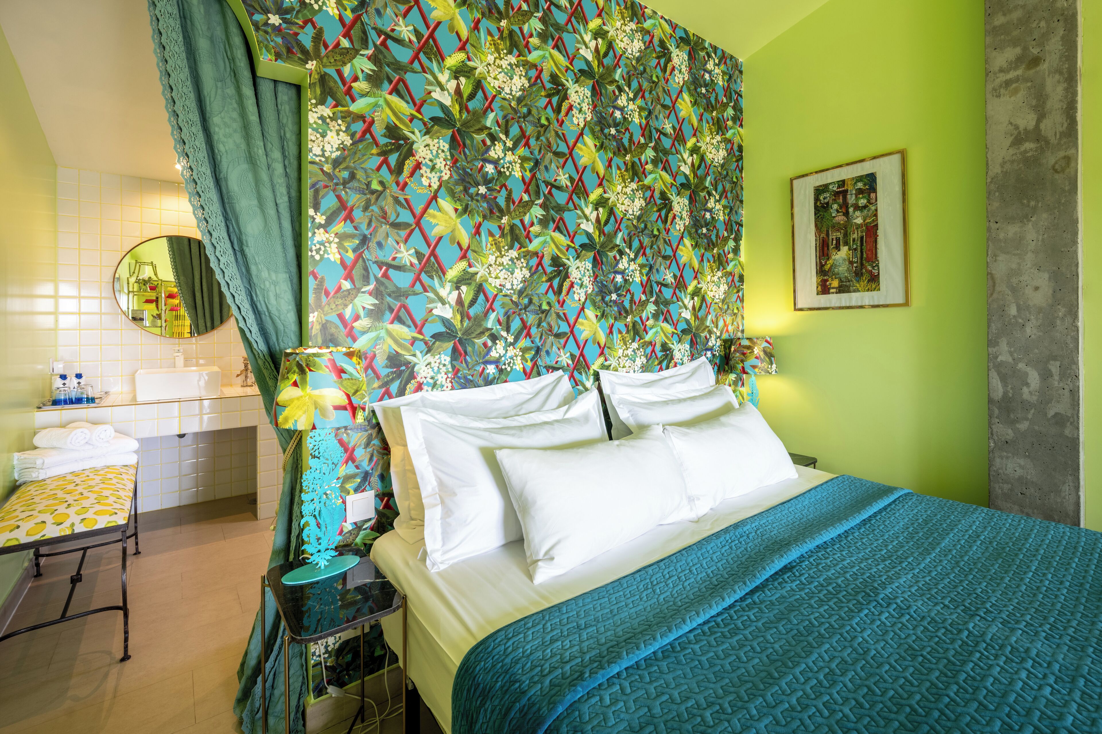 A hotel room with a bed, a bedside table, a mirror, and a colorful wall pattern.