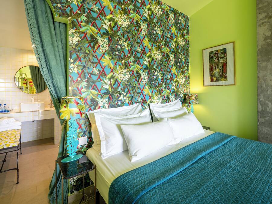 A hotel room with a bed, a bedside table, a mirror, and a colorful wall pattern.
