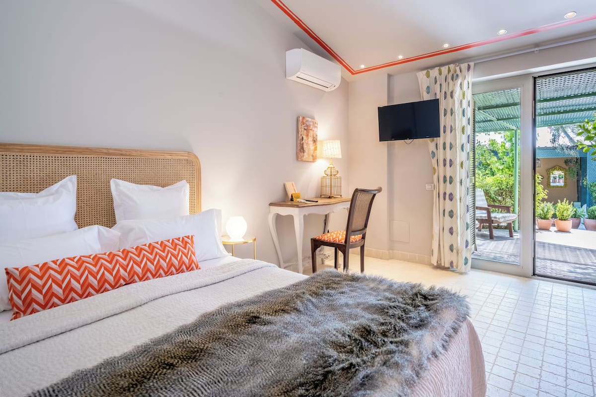 A modern hotel room with a large bed, a desk, and a view of the outdoor garden.