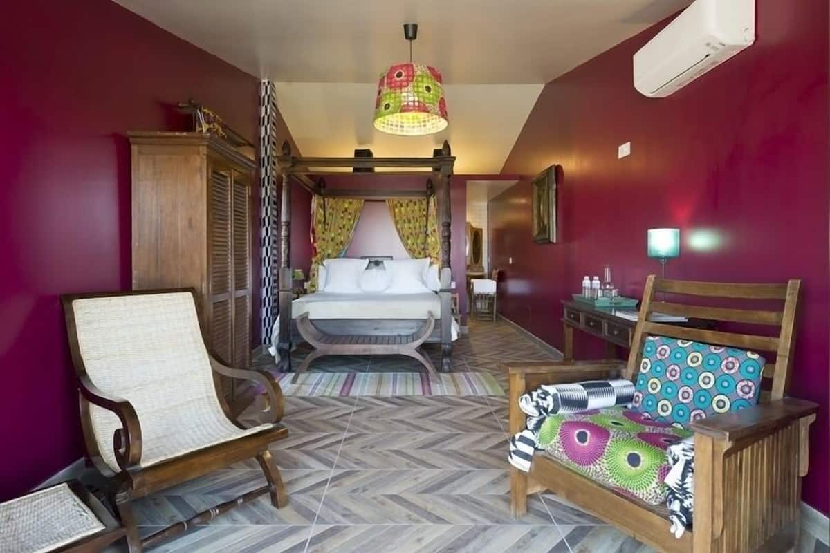 A hotel room with a bed, a chair, a table, a lamp, and a wall-mounted air conditioner.