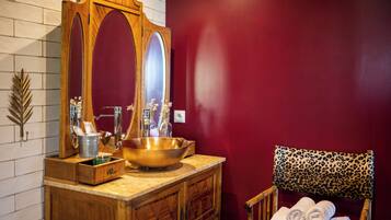 Un baño con tocador de madera, un espejo grande, un lavabo dorado y una silla de estampado de leopardo con toallas.