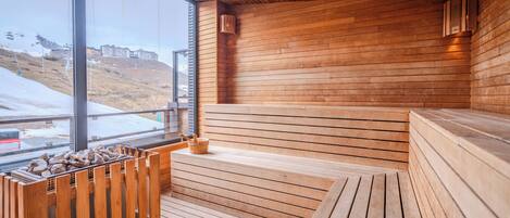 Un sauna en bois offrant une vue sur un paysage enneigé grâce à de grandes fenêtres.