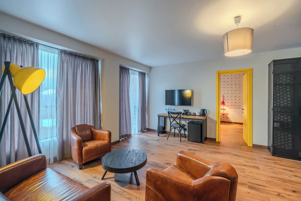 Una habitación de hotel moderna con sofás de cuero, una mesa de centro redonda, un escritorio con una computadora, un televisor y una cocina.