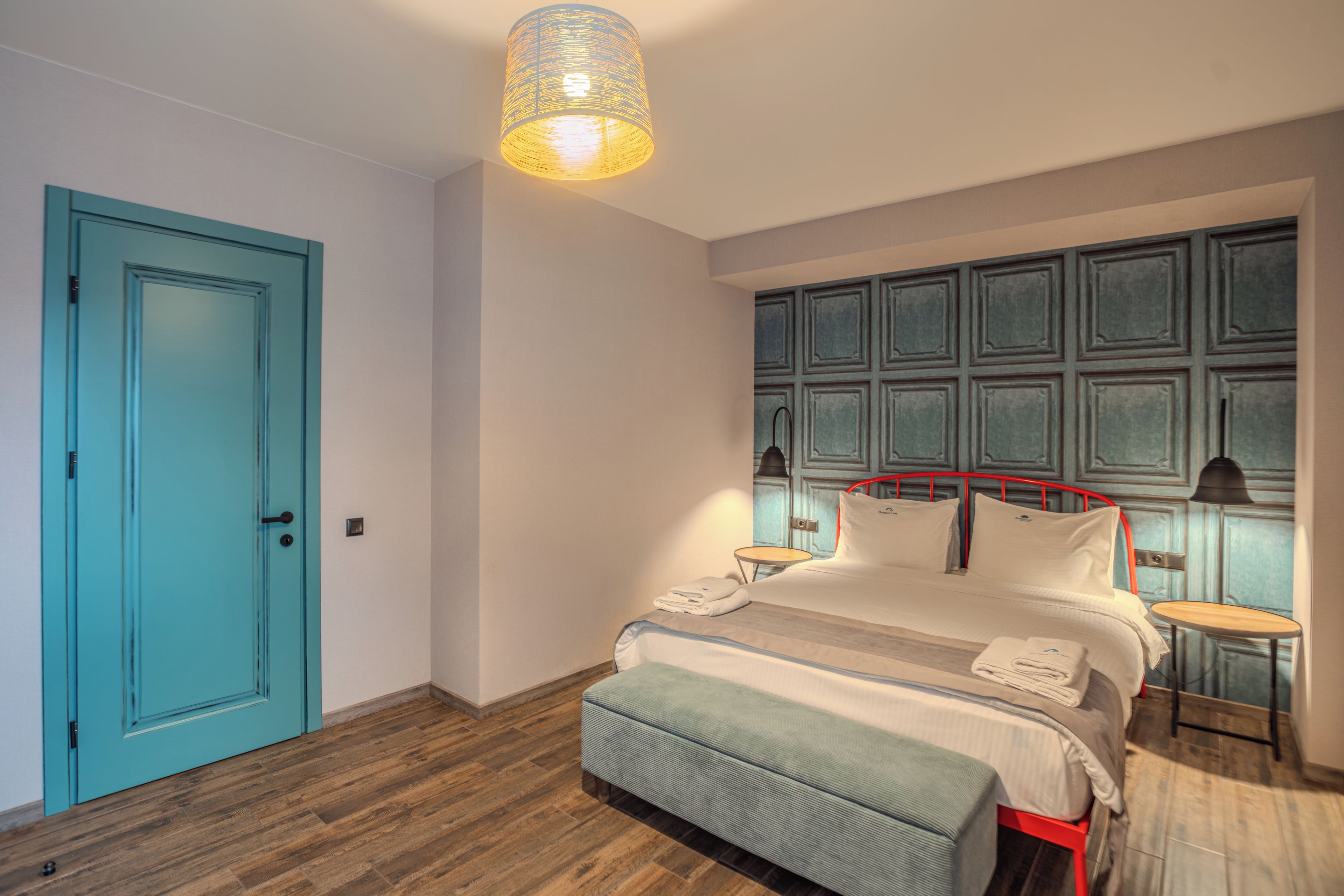 Een slaapkamer met een bed, nachtkastjes, een deur en een hanglamp.