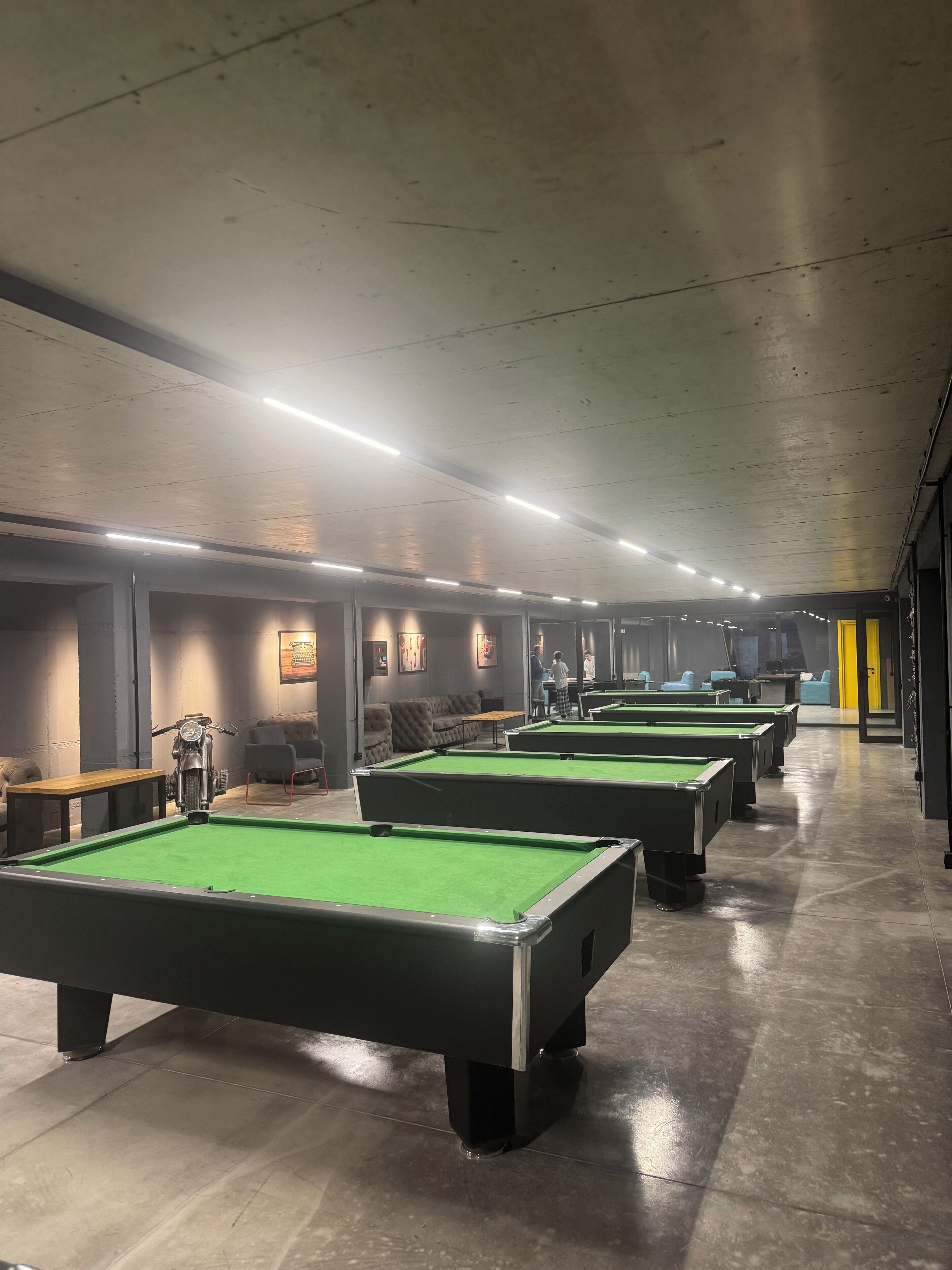 A pool hall with multiple pool tables, a motorcycle, and a sofa.