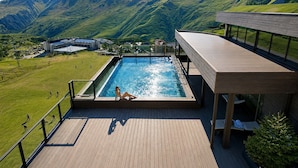 A pool with a view of mountains, a deck area, and a building in the background. - Gudauri Loft (Kazbegi)