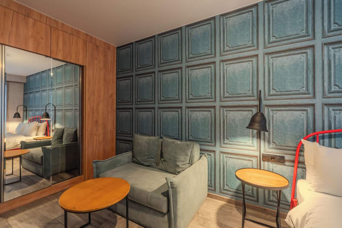 Una habitación moderna con piso de madera, un sofá verde, una pequeña mesa de madera, una lámpara roja y un espejo grande.