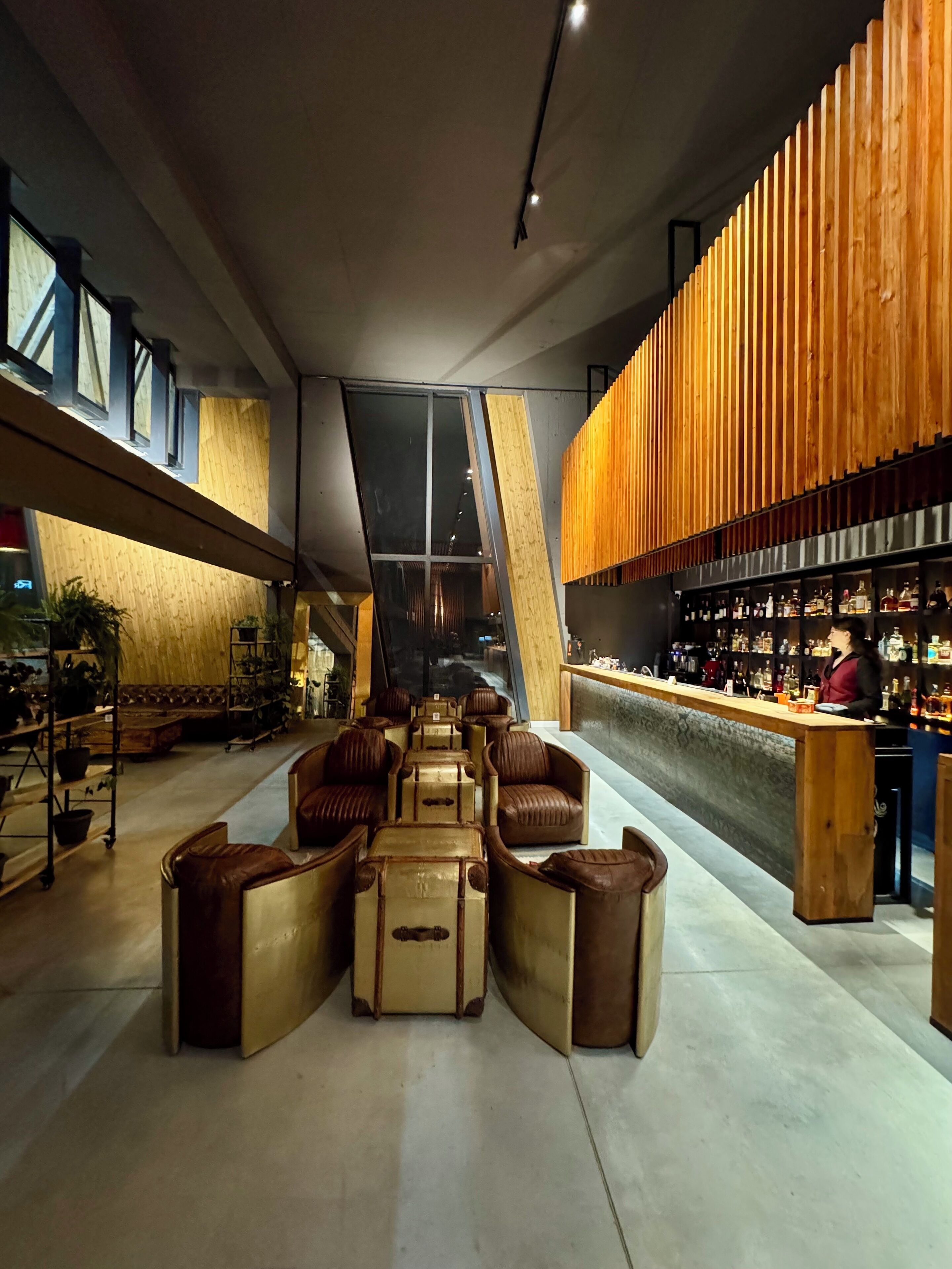 A modern bar area with leather seating, a wooden slatted wall, and a bar stocked with bottles.