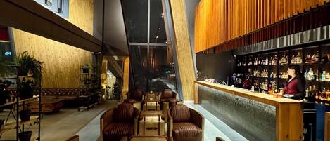 Zona de bar moderna con asientos de cuero, pared de listones de madera y barra provista de botellas.