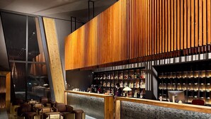 A modern bar area with a wooden slat wall, seating with luggage, and a bar counter with a variety of bottles. - Gudauri Loft (Kazbegi)