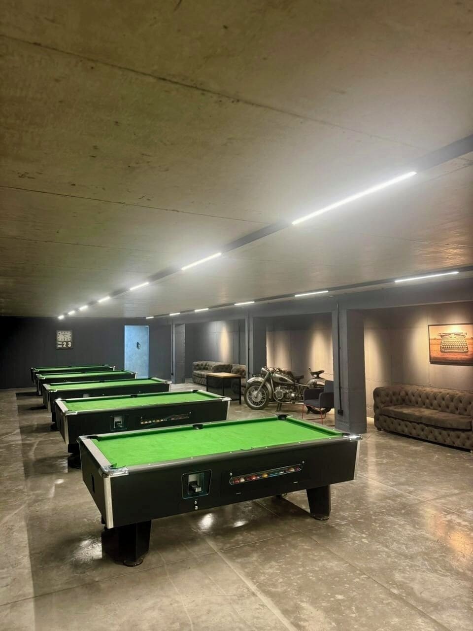 A pool hall with multiple pool tables, a motorcycle, and a couch.