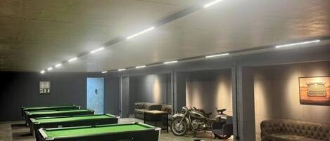 A pool hall with multiple pool tables, a motorcycle, and a couch.