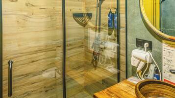 Una doccia vetrata con interni in legno, un mobile bagno in legno con lavabo a bacinella e uno specchio con cornice gialla.