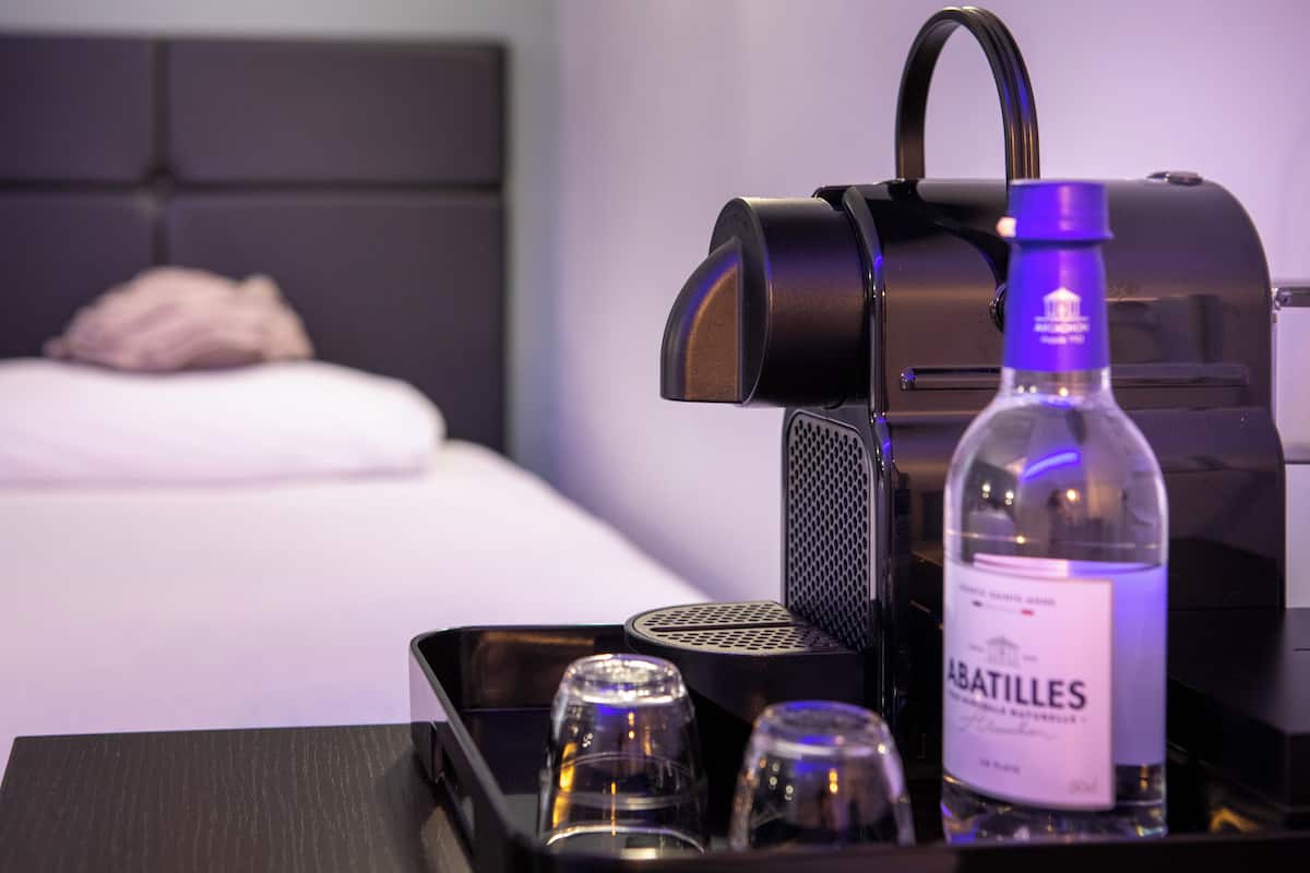 A minibar with a bottle of Abatilles wine, a glass, and a glass of water.