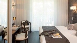 A hotel room with a bed, a desk, two chairs, a lamp, and a window with sheer curtains. - Hotel Le Relais de Farrou (Saint-Remy)