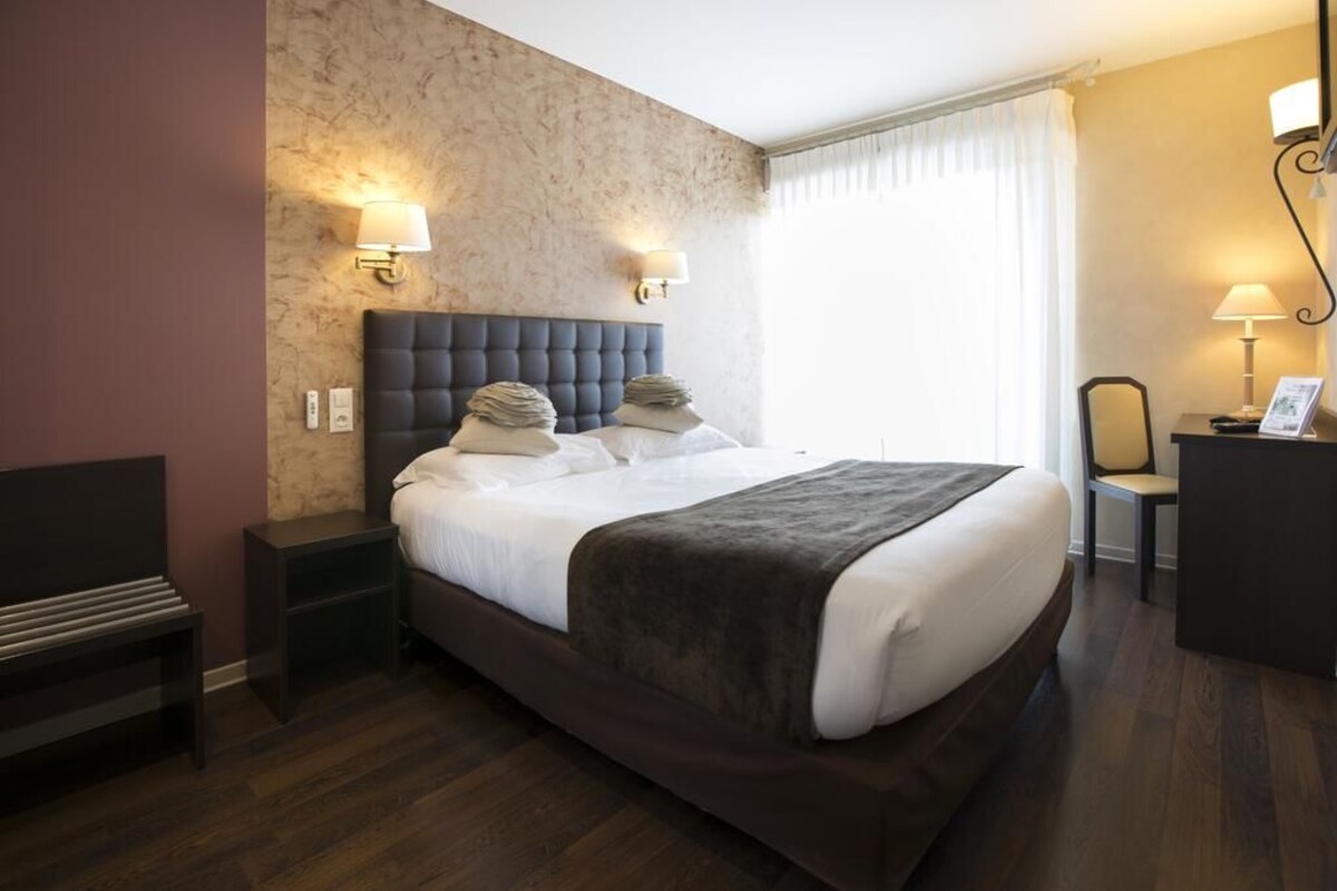 A hotel room with a large bed, two bedside tables, a desk, and a chair.
