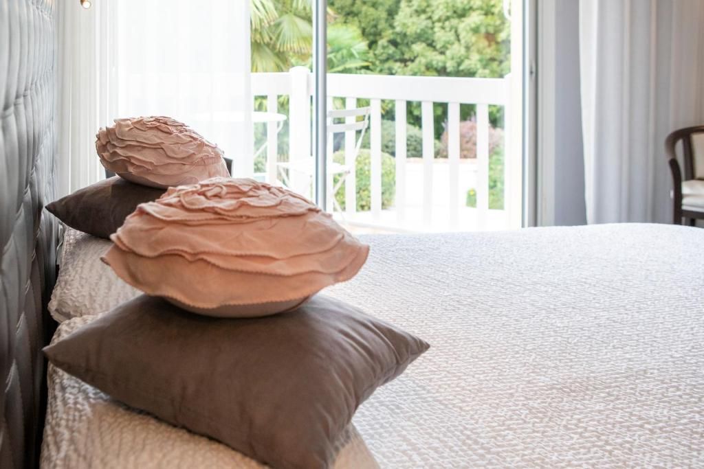 A bed with a textured white cover, two brown pillows, and a view of a white balcony with greenery outside.