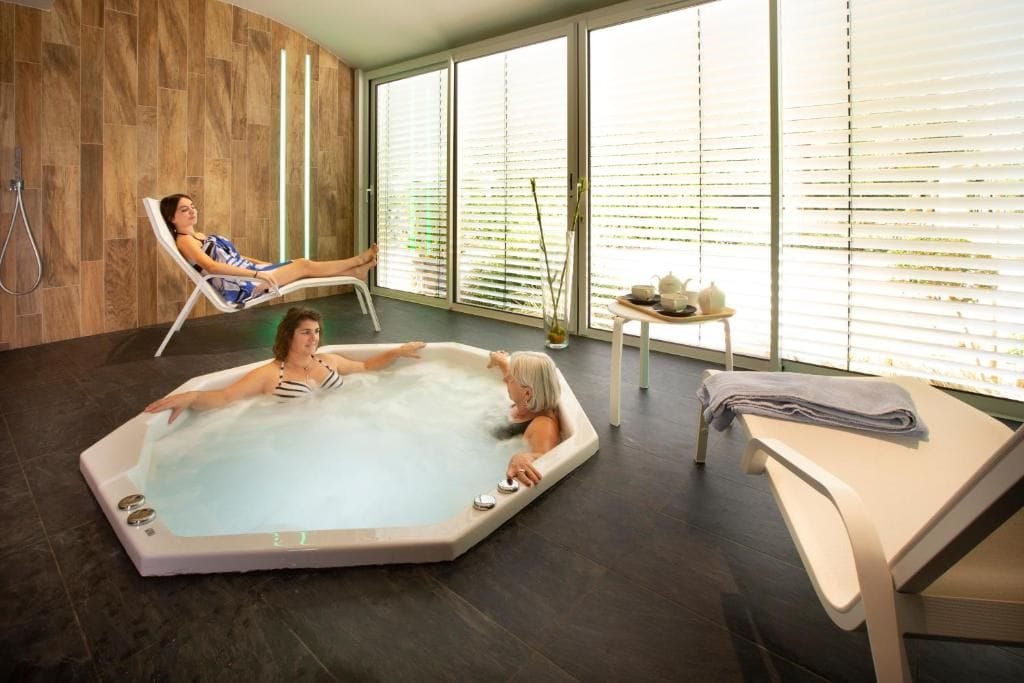 Uma área interna de piscina moderna, com uma espreguiçadeira e uma banheira de hidromassagem.