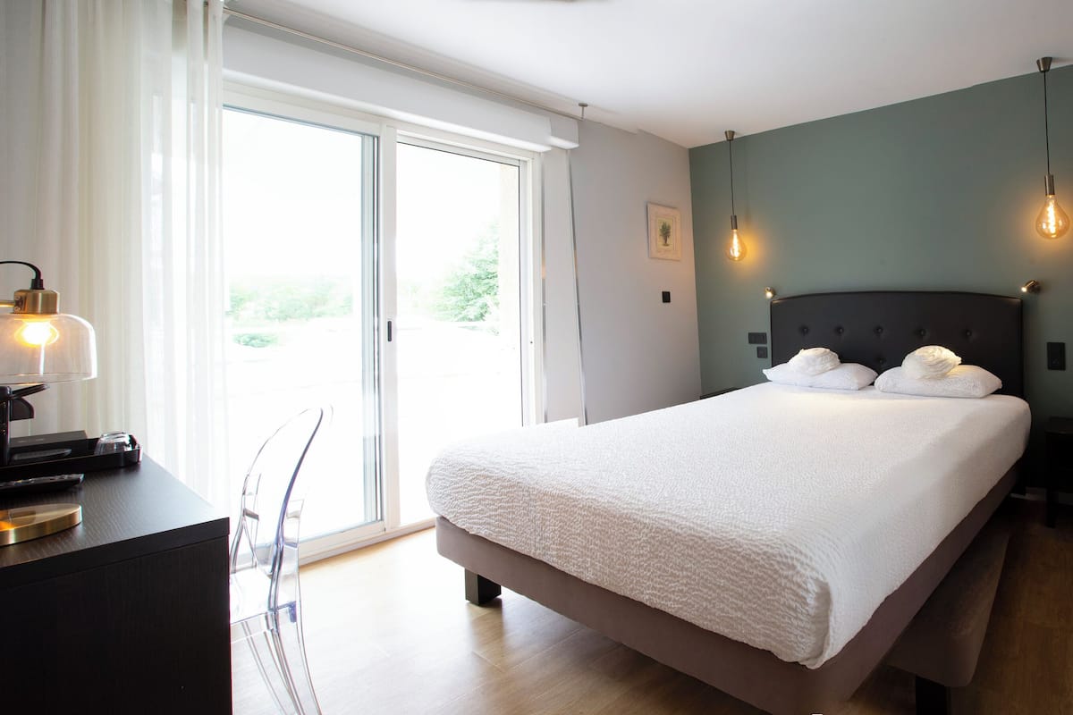 A modern bedroom with a large bed, a desk with a lamp, and a bench.
