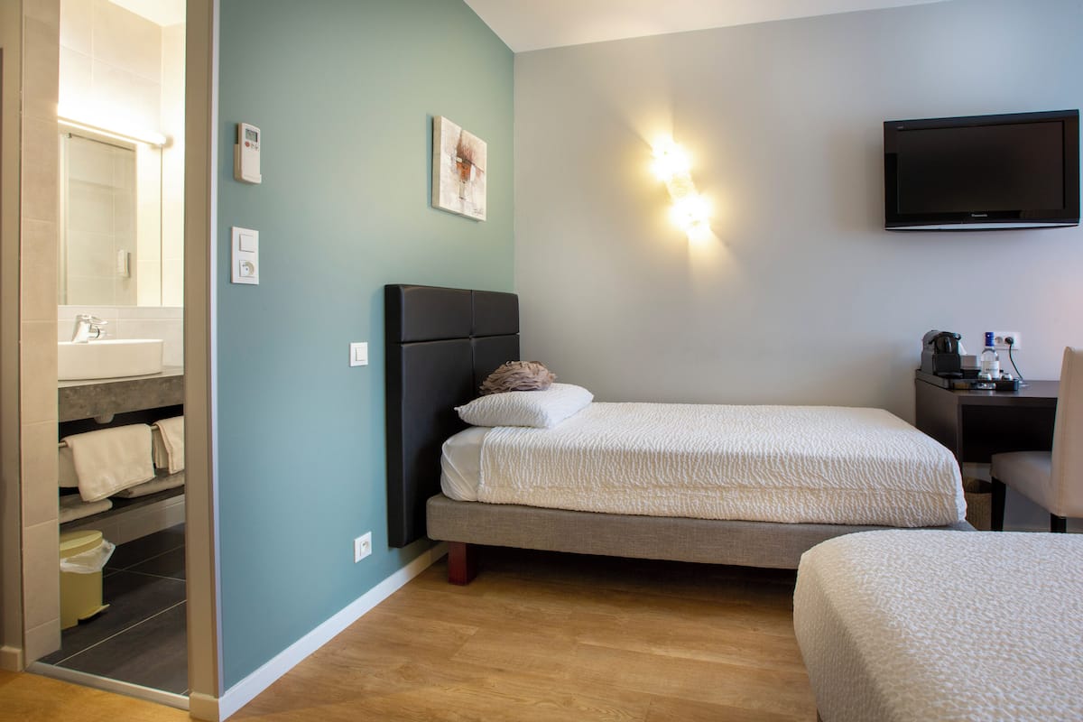 A hotel room with two beds, a bathroom with a mirror, and a TV mounted on the wall.