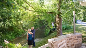 A stone bench with a metal post, surrounded by lush greenery and a small stream. - Hotel Le Relais de Farrou (Saint-Remy)