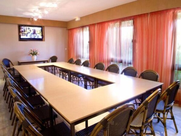 A conference room with a long table and chairs, a television on the wall, and large windows with curtains. - Hotel Le Relais de Farrou (Saint-Remy)