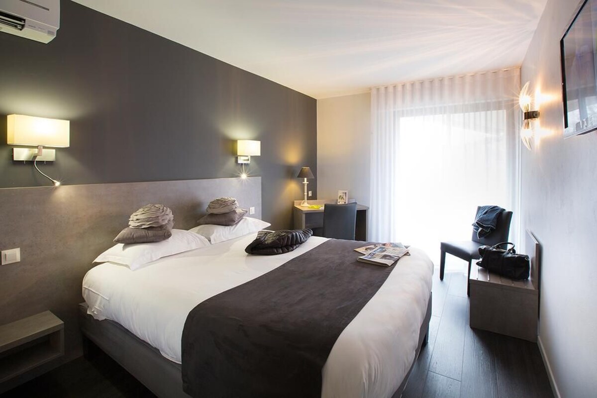Quarto de hotel com uma cama grande, mesas de cabeceira, uma escrivaninha e uma cadeira.