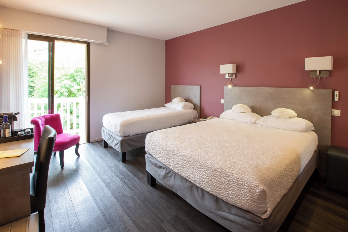 A hotel room with two beds, a desk, a chair, and a balcony with a view.