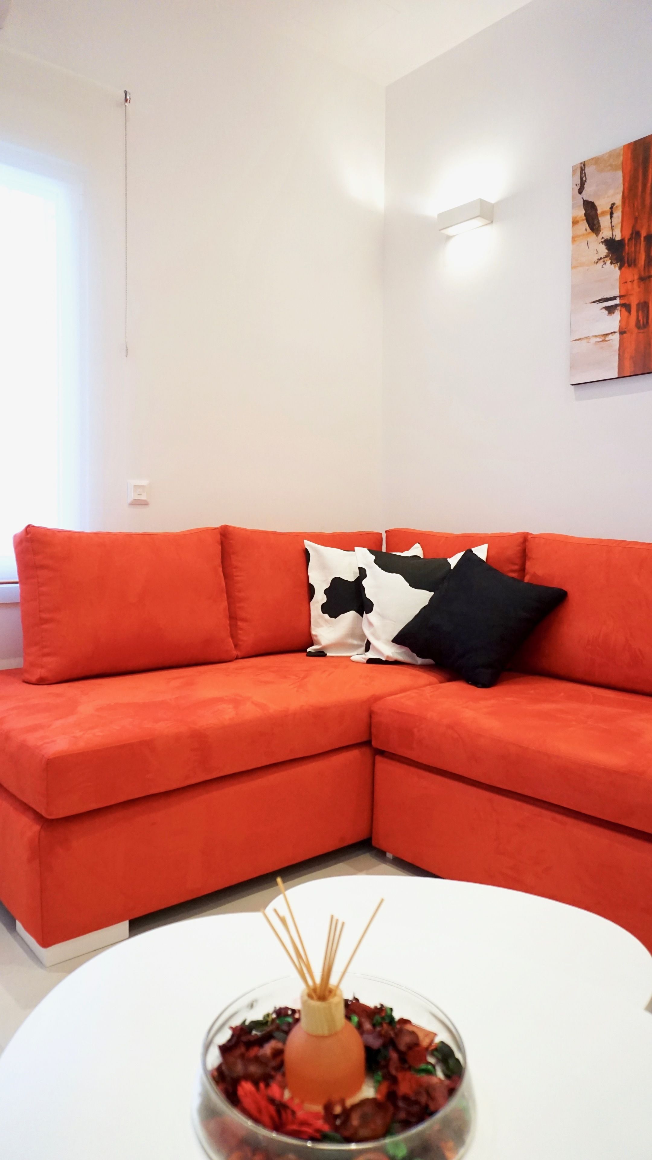 A modern living room with a red sectional sofa, a white coffee table with a decorative centerpiece, and a minimalist wall with a single artwork.