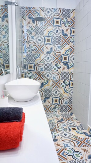 Un baño con lavamanos blanco, ducha y azulejos estampados.