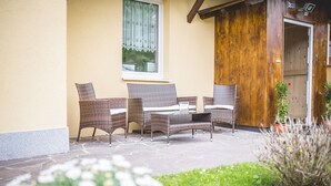 An outdoor seating area with wicker furniture and a stone floor. - Ferienwohnung Alpi (Garmisch-Partenkirchen)
