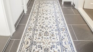 A hallway with a patterned rug, white walls, and a bench with a vase of flowers. - Ferienwohnung Alpi (Garmisch-Partenkirchen)