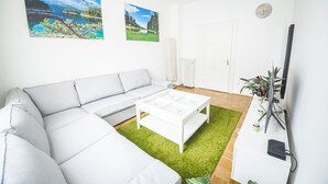 A modern living room with a white sofa, a white coffee table, and two landscape paintings on the wall. - Ferienwohnung Alpi (Garmisch-Partenkirchen)