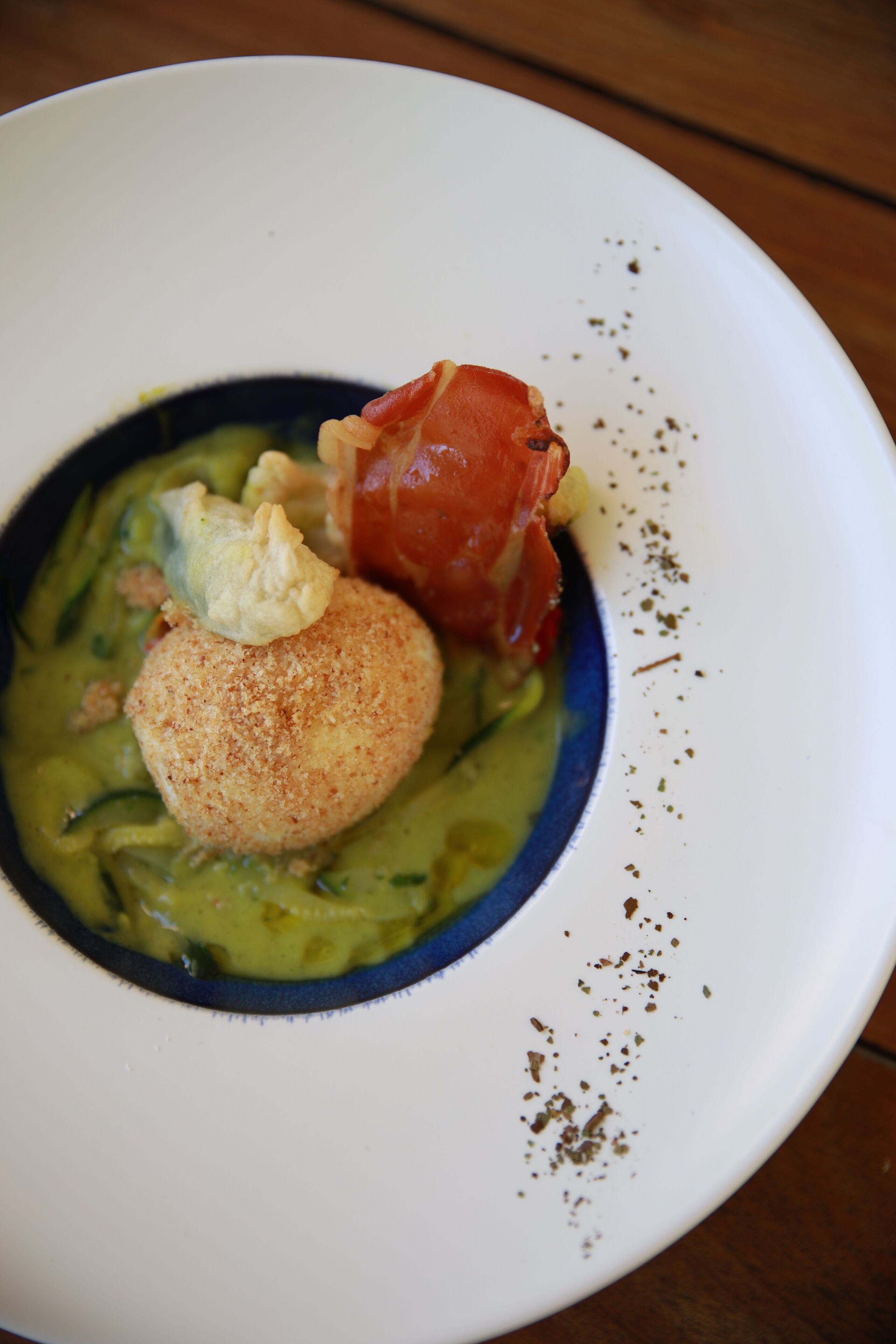 A bowl of food with a green sauce, a round breaded item, and a piece of red meat on a white plate.