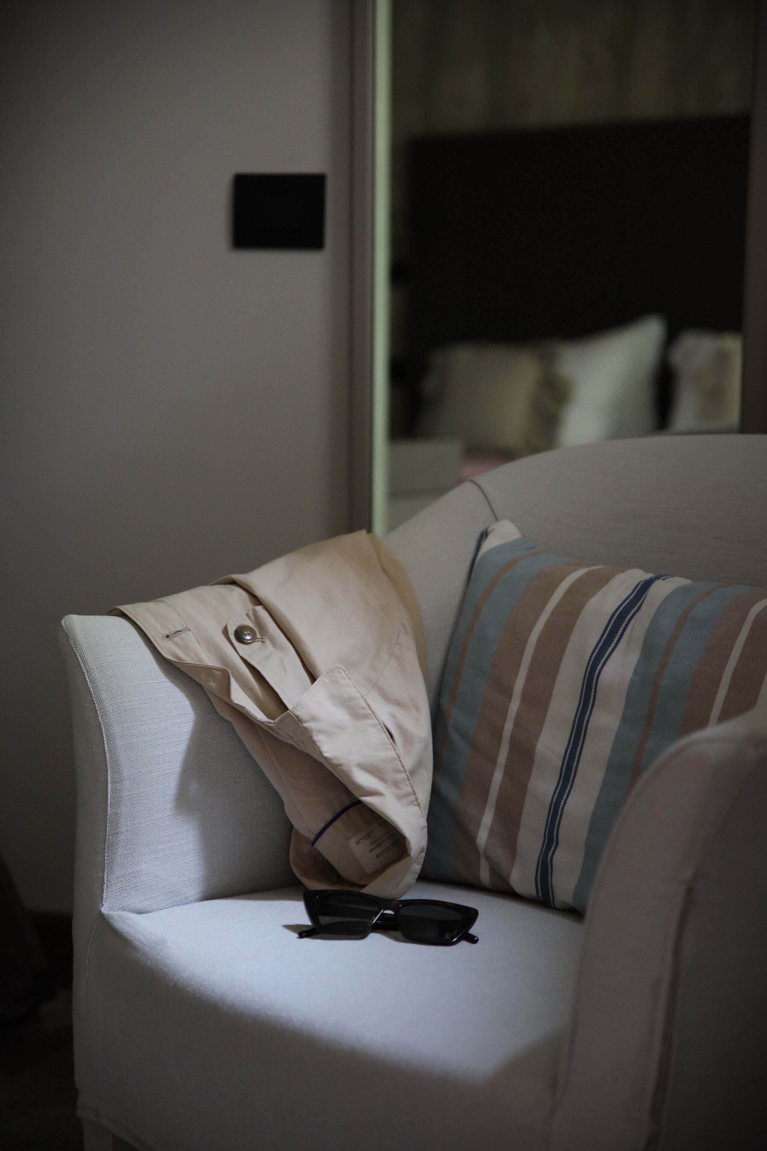 Un coin de pièce avec un canapé de couleur claire, un coussin à rayures et une paire de lunettes posée sur l’accoudoir.