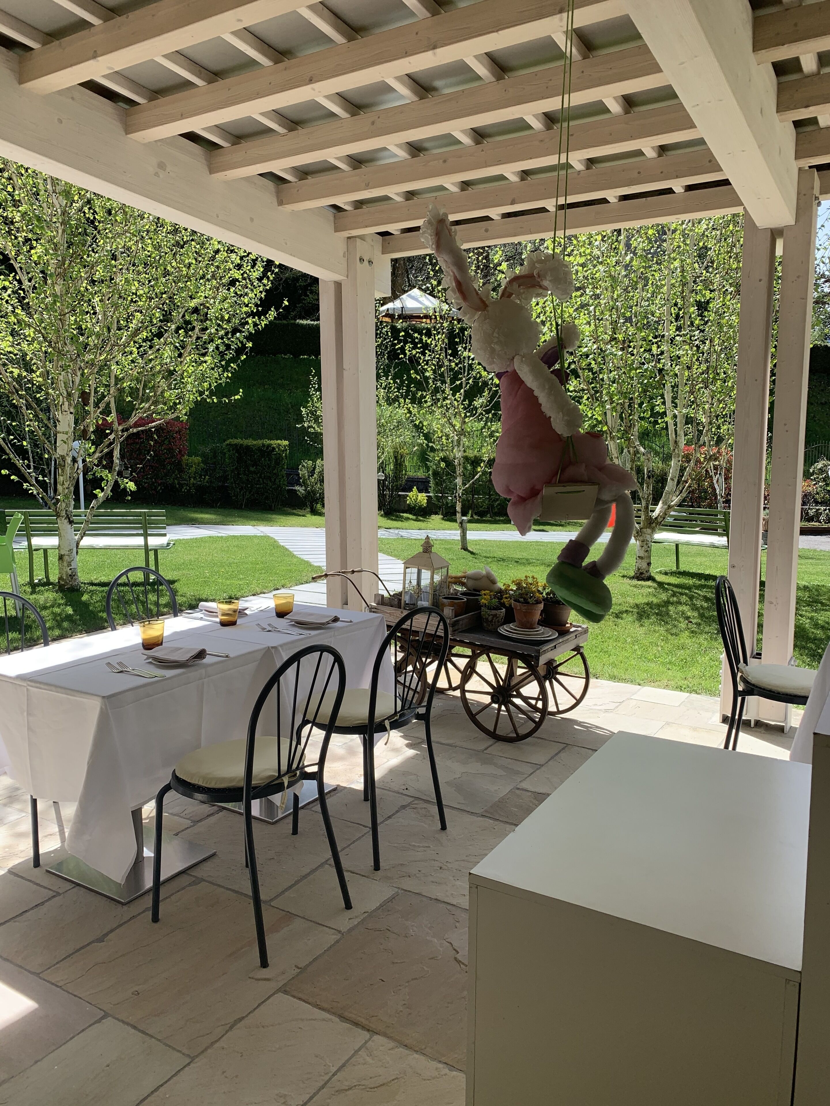 Eine Außenpatio-Terrasse mit überdachter Sitzgelegenheit, einem Esstisch und einem dekorativen Wagen mit Blumentöpfen.