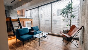 A modern living space with a loft bed, blue sofa, leather chair, and a large window with blinds. - THE BEDROOM Daimyo (Fukuoka)