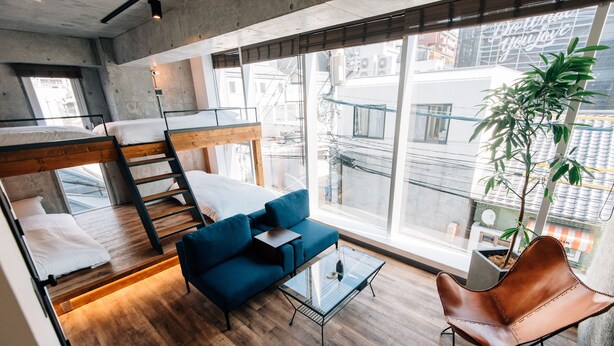 A modern loft-style room with a bunk bed, a blue sofa, a glass coffee table, and a leather armchair. - THE BEDROOM Daimyo (Fukuoka)