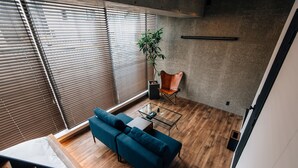 A modern living room with a blue sofa, wooden flooring, and a large window with blinds. - THE BEDROOM Daimyo (Fukuoka)