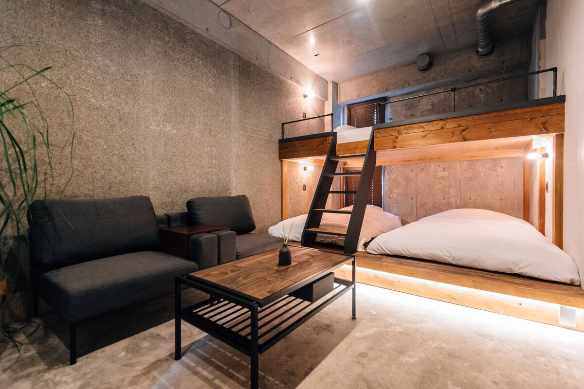 Una cama litera con cabecera de madera, un sofá, una mesita de centro y una planta.