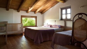Un dormitorio con dos camas, suelo de madera, techo inclinado y ventana con vista a follaje.
