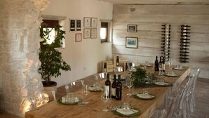 Una larga mesa de madera para comer con copas de vino, platos y botellas, rodeada de sillas transparentes.