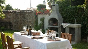 Una mesa de comedor al aire libre con un muro de piedra y un horno de ladrillo al fondo.