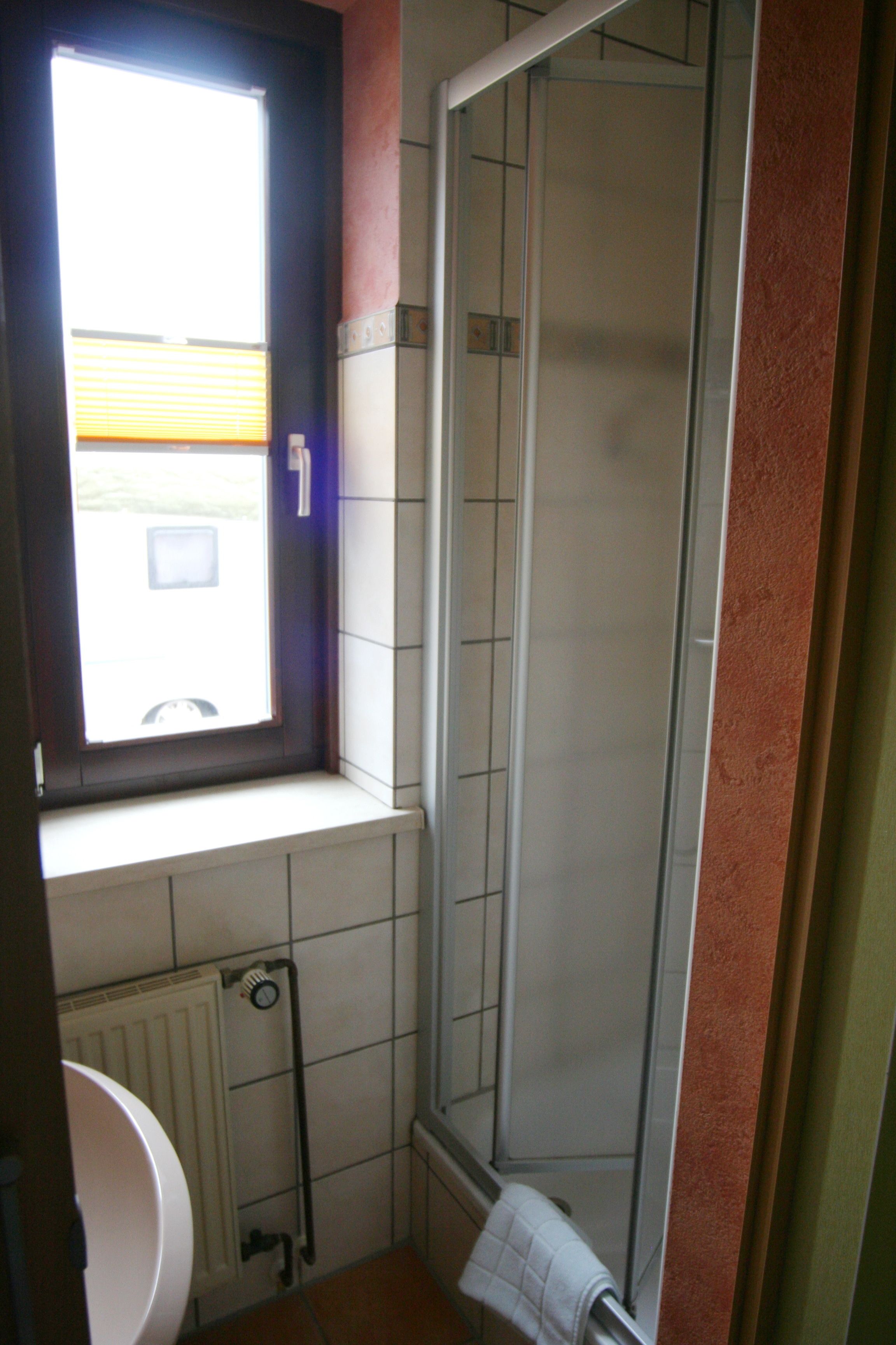 A bathroom with a window, a shower, and a radiator.