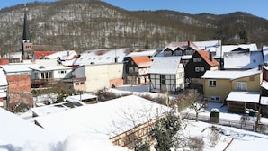 A snow-covered village with traditional half-timbered houses and a church steeple. - Gästehaus Tröbs (Harztor)