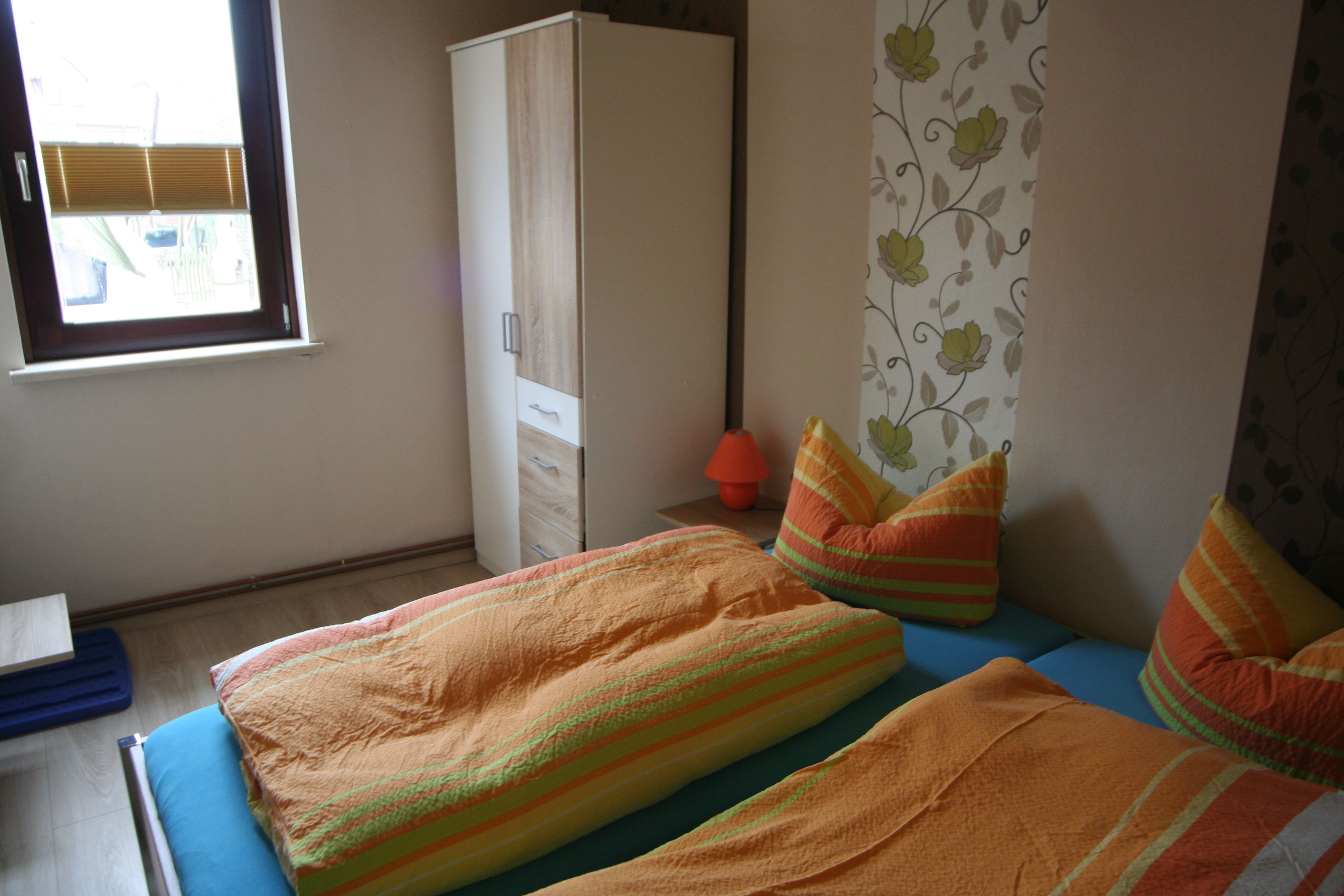 A bedroom with two beds, a wardrobe, a window, and a floral-patterned curtain.