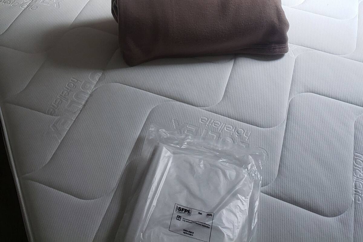 A neatly made bed with white pillows, a brown blanket, and a package on the mattress.