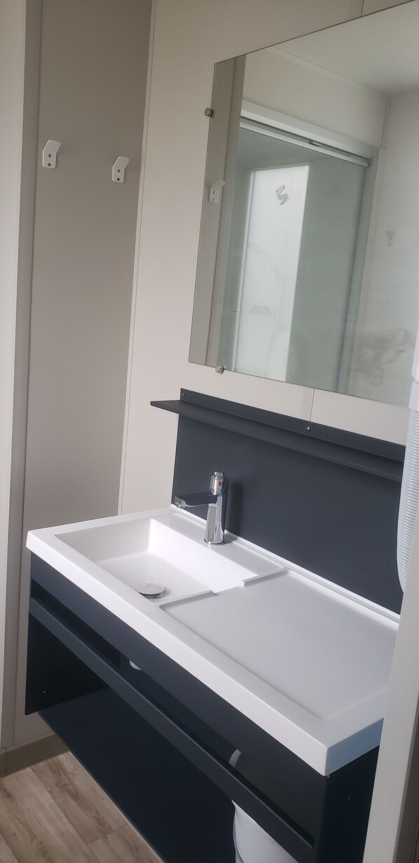 Un baño moderno con un lavamanos blanco, encimera oscura y un espejo encima.