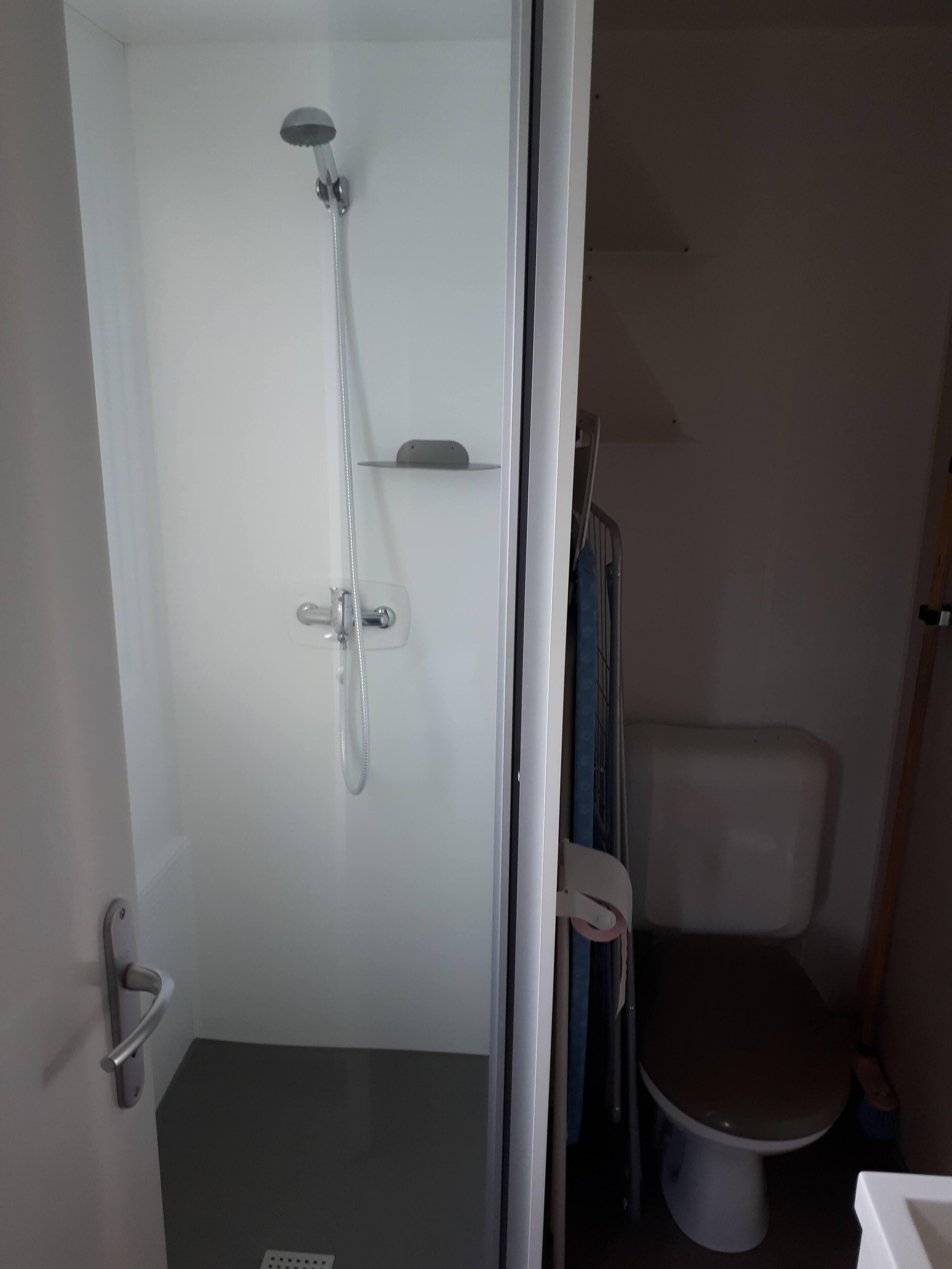 Une petite salle de bain fermée, équipée d’une douche, de toilettes et d’une étagère au-dessus des toilettes.